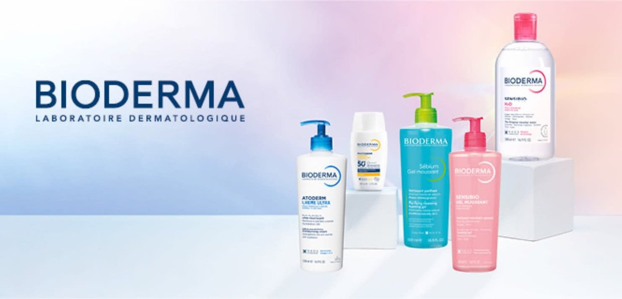 Produits de soin Bioderma avec des flacons blancs, bleus, verts et roses présentés sur des blocs blancs sur un fond dégradé bleu-rose.