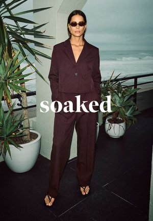 Burgundy cropped blazer with matching wide-leg trousers, textured fabric, slim fit, styled with black sunglasses and minimalist sandals.