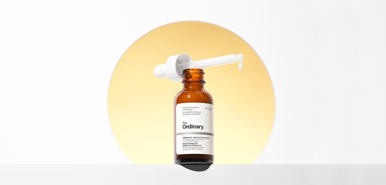 Botella cuentagotas de vidrio ámbar etiquetada como The Ordinary, con gotero que libera un líquido blanco, sobre un fondo circular amarillo suave.