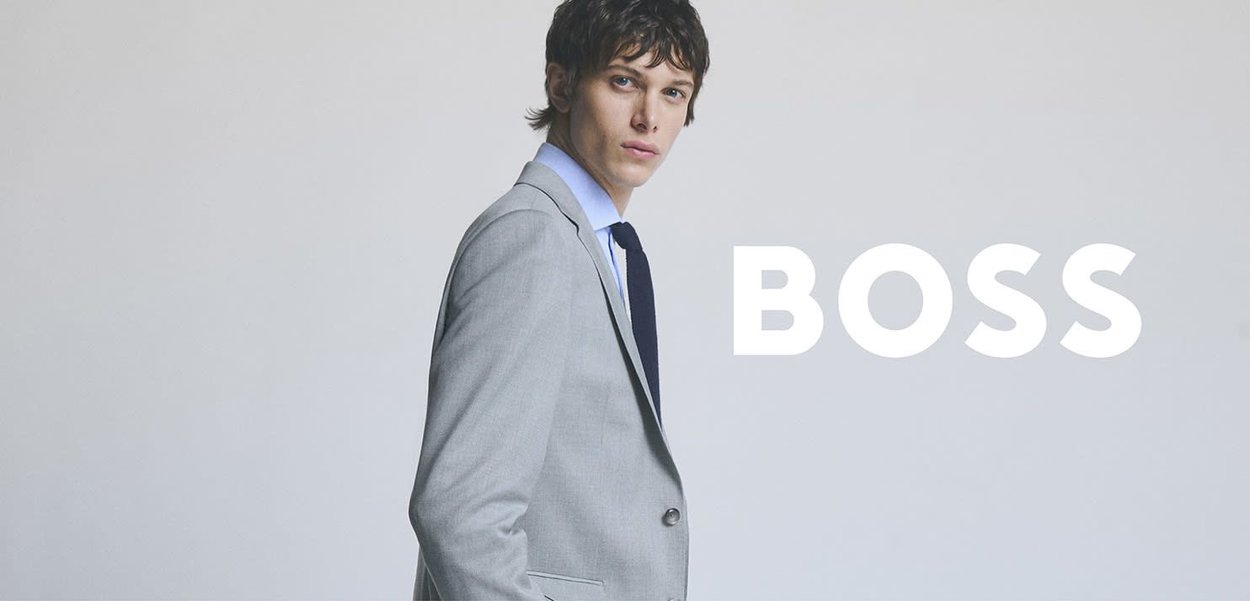Light gray suit with structured fit, notched lapels, and a single button closure, paired with a light blue shirt and dark tie.