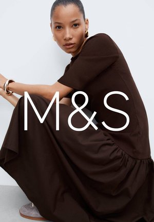 Robe marron côtelée avec un ourlet évasé et une légère brillance, associée à de grandes boucles d'oreilles dorées et un bracelet texturé. Fond neutre.