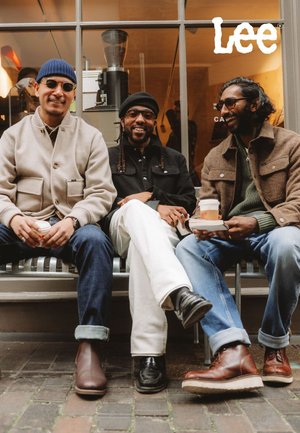 Drie mannen zitten op een bankje, elk met verschillende jassen en broeken aan. Opvallend schoeisel zijn bruine laarzen en zwarte schoenen. De omgeving suggereert een café.