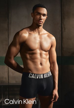 Schwarze Baumwoll-Boxershorts mit einem weißen Logo-Bund, die eine enge Passform und Flachnähte aufweisen, präsentiert an einem Modell mit athletischer Figur.