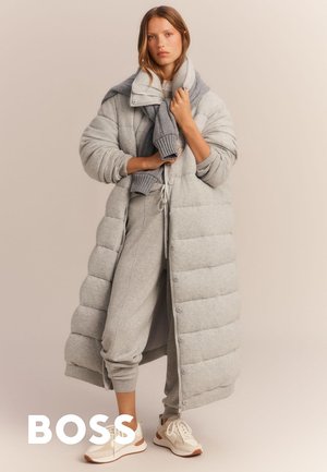 Ljusgrå puffjacka med en texturerad yta, tillsammans med en matchande tröja och joggers. Cremfärgade sneakers med bruna accenter fulländar looken.