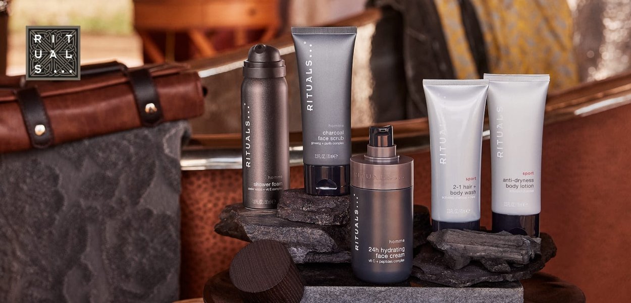 Produits de soins pour hommes Rituals exposés sur des pierres de charbon empilées avec un sac en cuir et un fond intérieur flou.