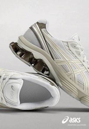Witte en beige sportschoenen met een bovenkant van mesh, een gevoerde zool en gebogen, glanzende accenten. Beschikt over een kenmerkend schokabsorberend hielontwerp.