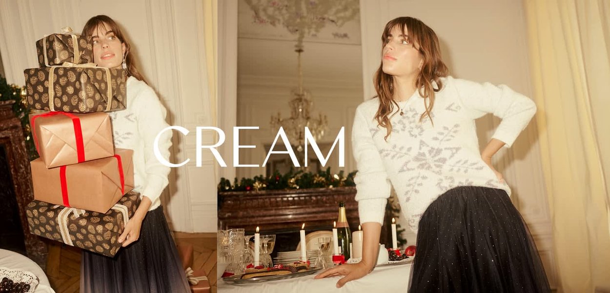 Weißer Pullover mit Schneeflockenmuster, schwarzer Tüllrock, gestapelte Geschenkkisten in Braun und Gold mit roten Bändern, festliche Tischdekoration im Hintergrund.