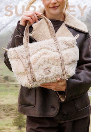 Borsa in finta pelliccia color beige cremoso con motivo testurizzato, manici in pelle e logo impresso. Presenta una superficie morbida e soffice e un design spazioso.