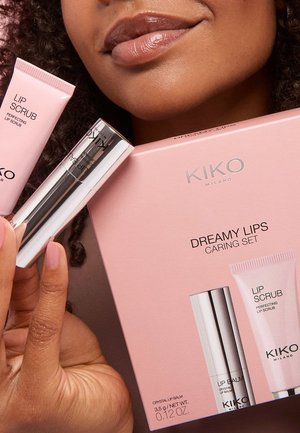 Primo piano di una persona che tiene il Kit Cura Labbra Dreamy Lips di KIKO Milano con scrub per labbra e balsamo labbra in tubo argentato vicino alle sue labbra lucide.