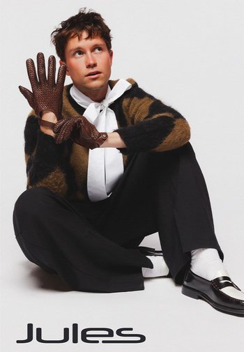 Gants en cuir marron avec un motif texturé, pull oversized à rayures noires et marron, nœud papillon blanc, pantalon noir et chaussures noires brillantes.