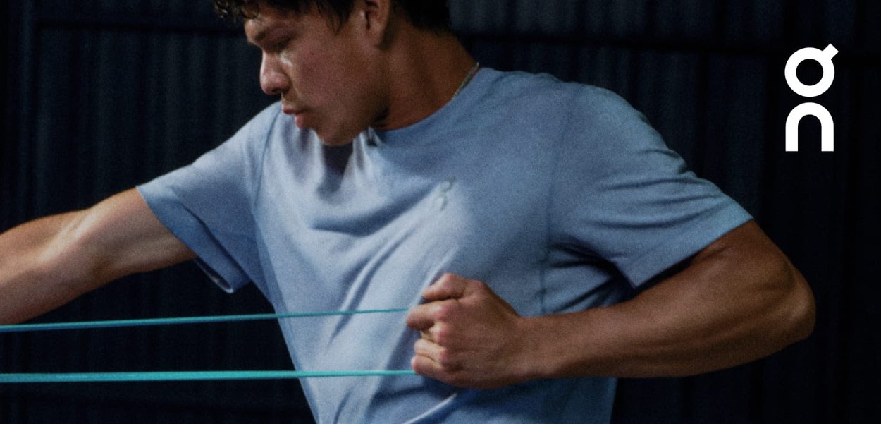 Sportliches T-Shirt aus hellblauem Stoff, taillierter Schnitt. Die Person verwendet Widerstandsbänder, was die Muskeldefinition und Bewegung zur Schau stellt.