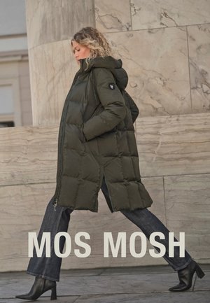 Long puffer coat in dark green, featuring a hood, quilted design, and side slits. Worn with dark jeans and heeled boots.
