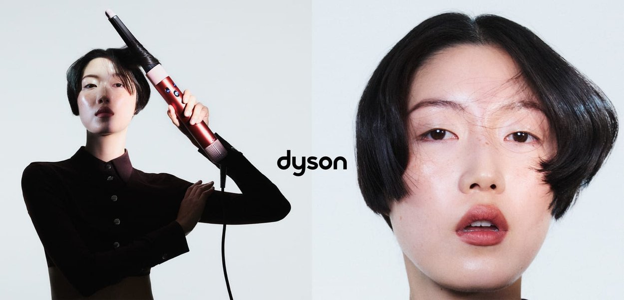 Strumento per acconciare i capelli Dyson in rosso e argento tenuto da una modella con un taglio bob elegante e pelle liscia, su uno sfondo neutro.