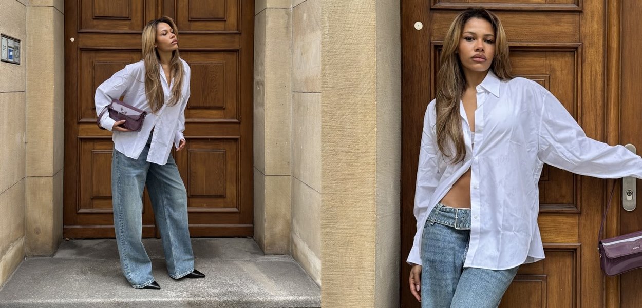 Camisa blanca abotonada, corte holgado, combinada con vaqueros de pierna ancha en azul claro. Bolso morado y zapatos negros puntiagudos. Puerta de madera al fondo.