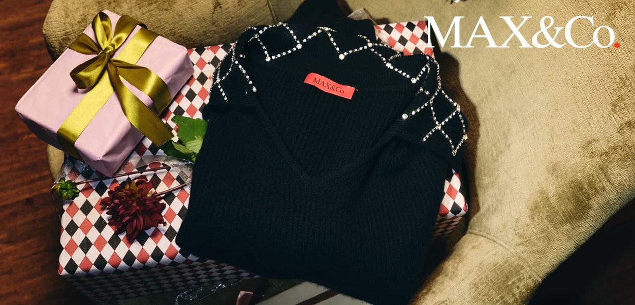 Pull noir avec détails en perles sur le col, plié sur des boîtes-cadeaux à motifs, avec un cadeau rose emballé avec un ruban doré.