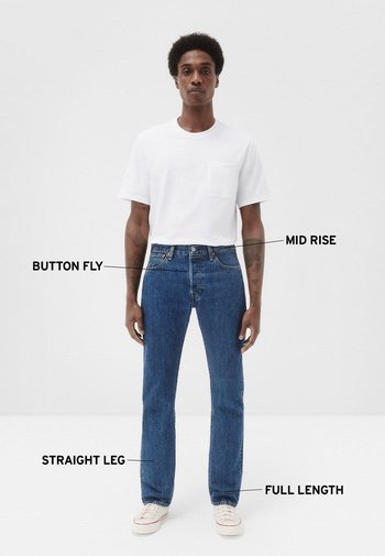 Jeans de mezclilla azul con una altura media, pierna recta, cierre de botón y corte a full, combinados con una camiseta blanca de manga corta.