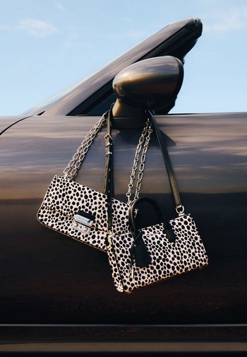 Two handbags in a pink and black leopard print, one with a chain strap and clasp, and the other with handles, resting on a car door.