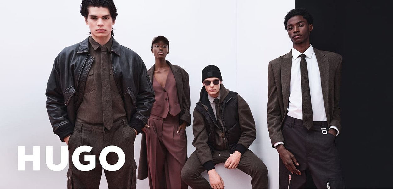 Vier Modelle tragen vielfältige Outfits: eine Lederjacke, maßgeschneiderte Anzüge und Texturen in gedämpften Farben. Verschiedene Accessoires verleihen den Stilen das gewisse Etwas.