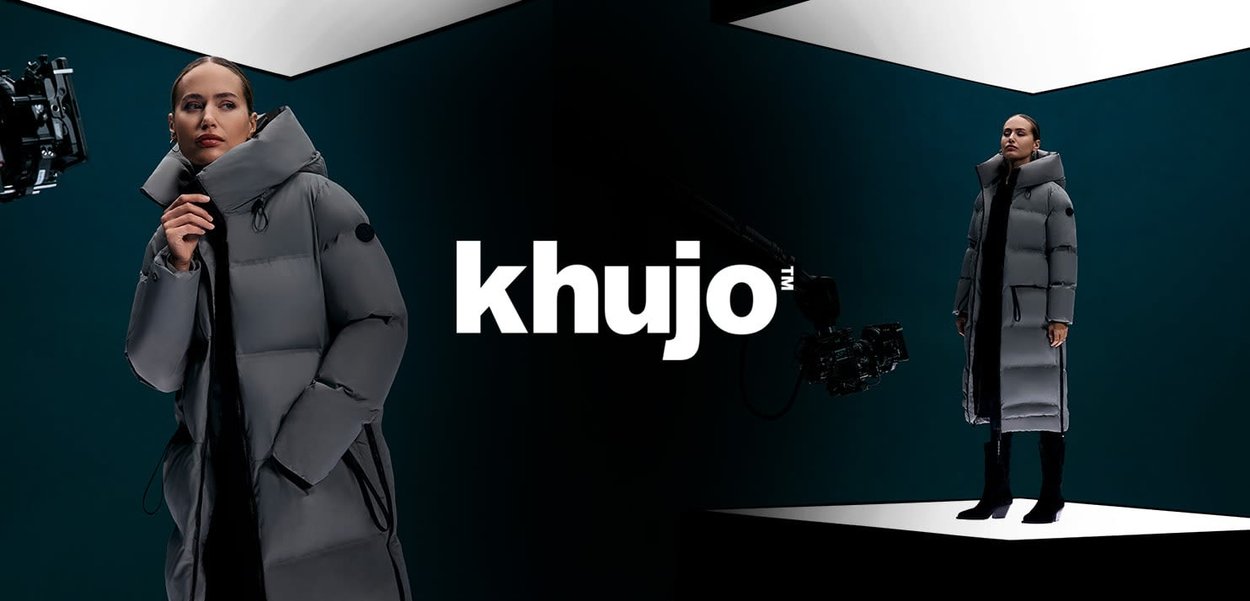 Vuorattu harmaa parkatakki korkealla kauluksella, jossa musta korostelogolla, esitetty studiokuvassa, jossa on kontrastisia geometrisia taustoja.