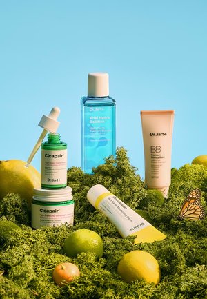 Dr.Jart+ skincare products including Cicapair serum and cream, Vital Hydra Solution essence, Ceramidin cream, and BB balm on green moss with citrus fruits.