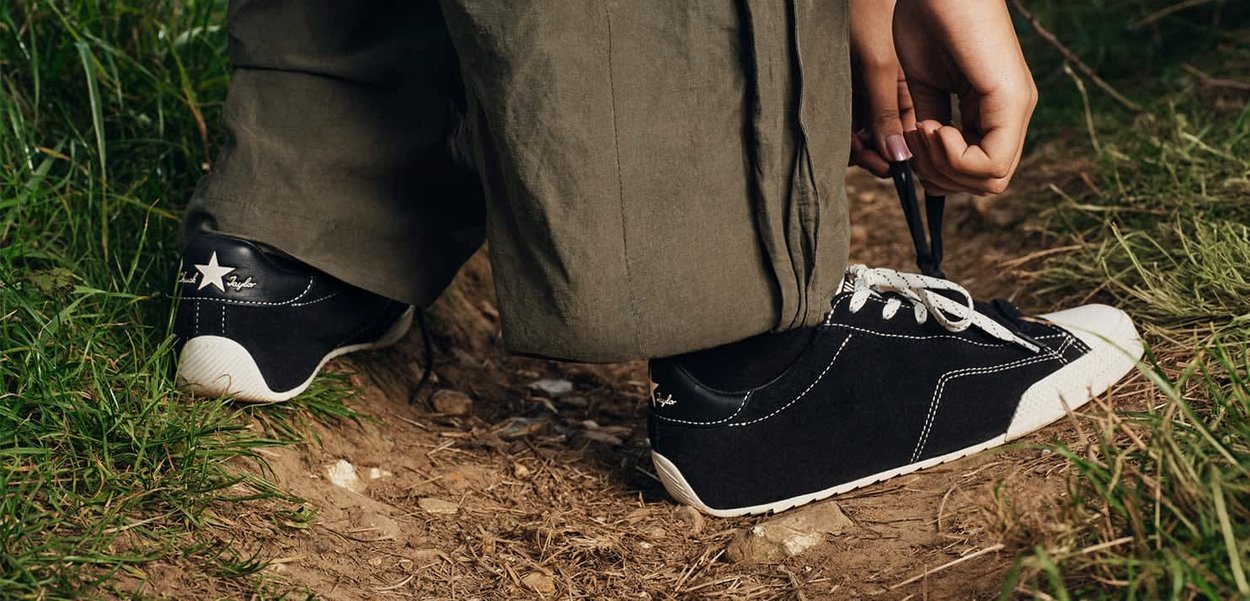 Persona che allaccia scarpe da ginnastica bianche e nere mentre si trova su un sentiero sterrato circondato da erba.