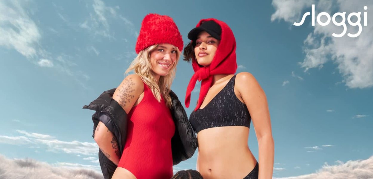 Due modelle in costume da bagno: una con un intero rosso e l'altra con un bikini nero, entrambe indossano cappelli colorati a contrasto contro un cielo blu.