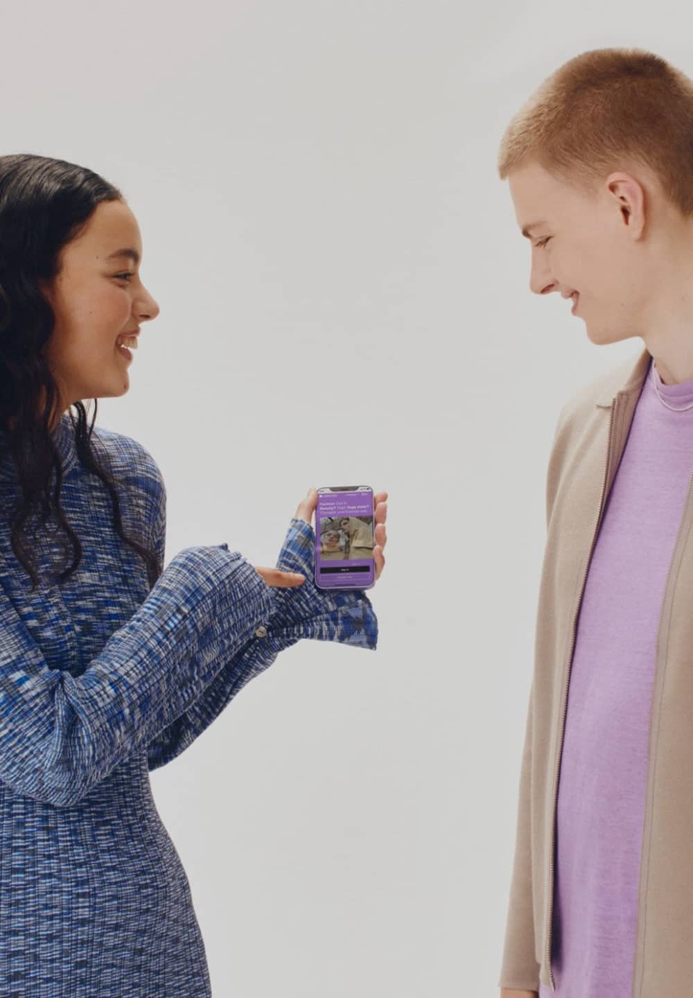 Smartphone con custodia viola mostrato da una persona in un vestito blu a fantasia, che mostra un'immagine e del testo sullo schermo.