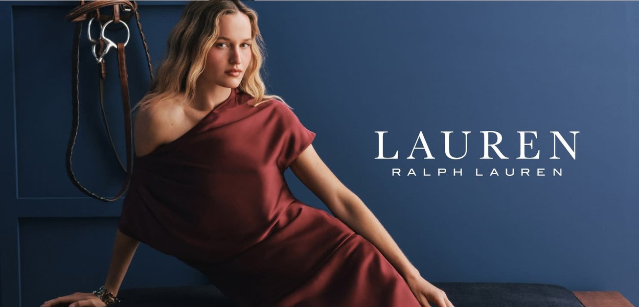 Bordeauxfarbenes Kleid mit asymmetrischem Ausschnitt, aus einem glatten Stoff gefertigt. Gestylt vor einem tiefblauen Hintergrund mit Reit-Themen-Akzenten.