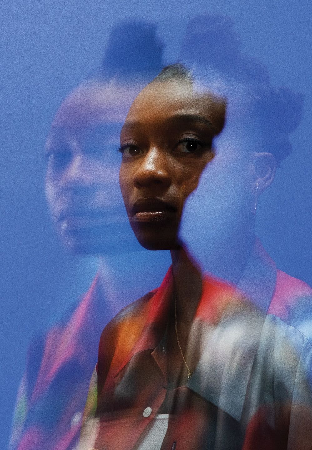 Porträt einer Person mit einem strukturierten, geschichteten Hintergrund. Die Person hat eine dunkle Hautfarbe und trägt ein buntes, knöpfbares Hemd mit einem kontrastierenden Kragen.