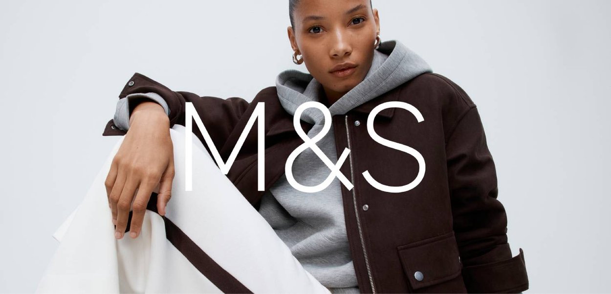 Veste marron avec un sweat à capuche gris en dessous, présentant une coupe décontractée et des détails métalliques visibles, associée à un pantalon clair.