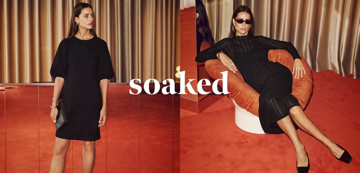 Black knit dress with a puffed sleeve and ribbed texture, paired with black pointed heels. A model sits on an orange accent chair.