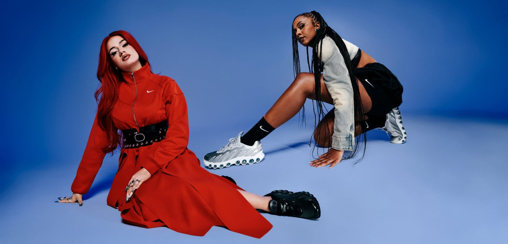 Rote Nike Zip-Jacke kombiniert mit einem schwarzen Gürtel und einem fließenden Rock. Zweites Model in einer Jeansjacke und schwarzen Shorts, trägt silberne Sneaker.