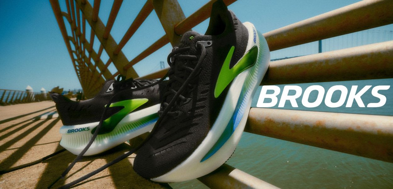 Zwarte hardloopschoenen met een gestructureerde bovenkant, met groene en blauwe accenten, en een dikke witte zool. Brandnaam "Brooks" duidelijk zichtbaar.