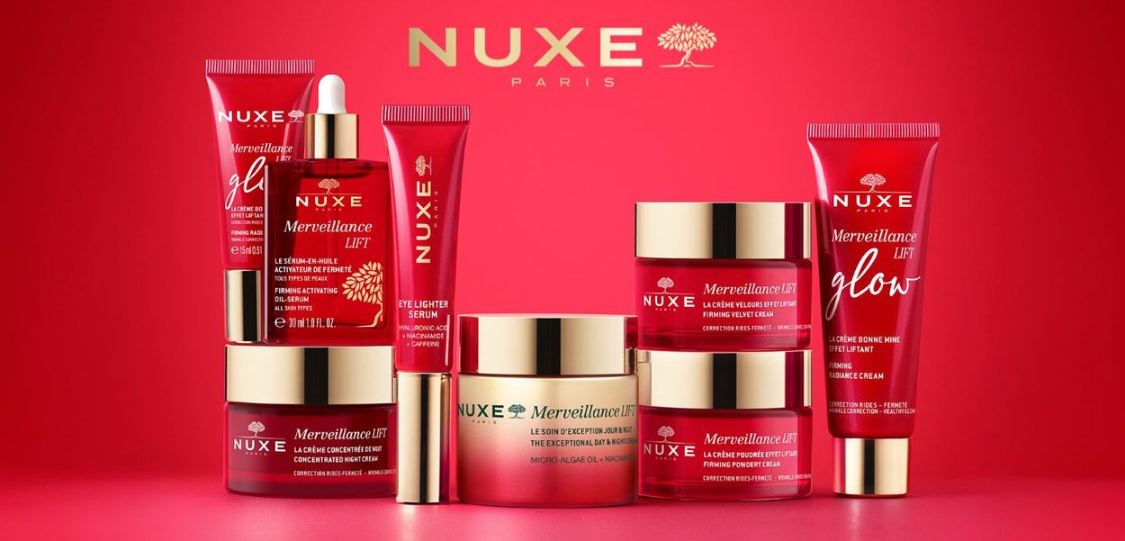 Collection de produits de soin NUXE avec un emballage rouge et or, comprenant des pots, des tubes et un compte-gouttes, disposés sur un fond rouge.