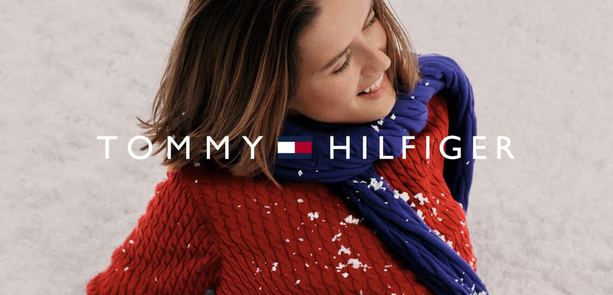 Pull en maille rouge avec une écharpe bleue, des flocons de neige visibles sur le tissu, arborant le logo Tommy Hilfiger bien en vue en dessous.