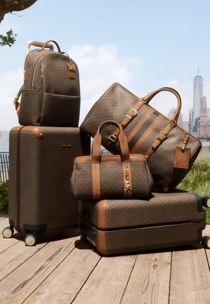 Ensemble de bagages bruns à motifs comprenant une valise, un sac fourre-tout, et un sac à dos avec des accents beiges, des fermetures éclair et des détails de logo, disposés en plein air.