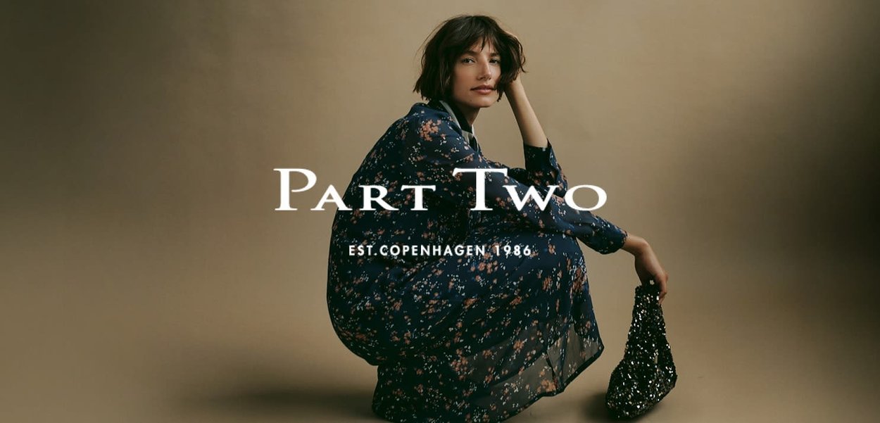 Fließendes dunkelblaues Kleid mit floralem Muster, weicher Textur und Dreiviertelärmeln. Modell hält eine glänzende schwarze Handtasche. Textüberlagerung beinhaltet "Teil Zwei."