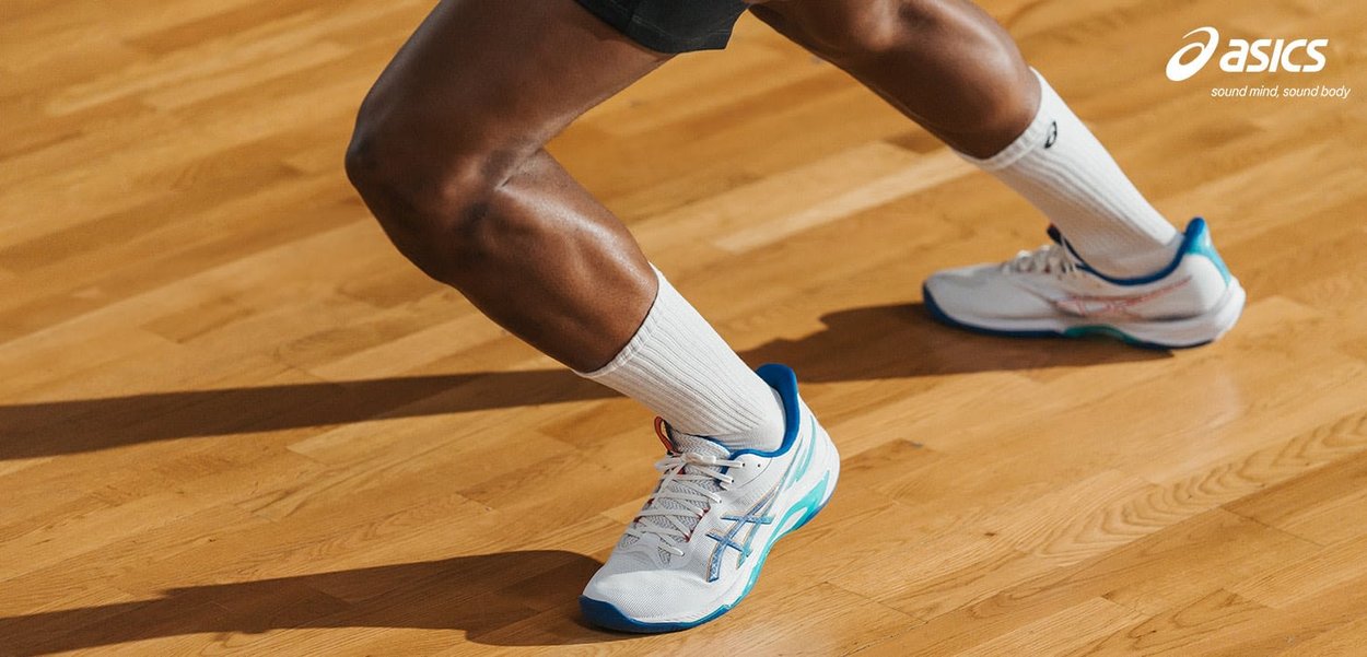 Idrettsutøvers ben i hvite Asics-sko og sokker som trår på en tre-gymgulv, merkevarelogo og slagord synlig i øverste høyre hjørne.
