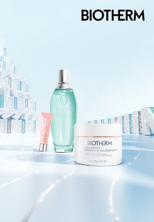 Produits de soin Biotherm : flacon vert transparent avec bouchon argenté, tube de crème rose, et pot blanc avec accent rose. Fond bleu.