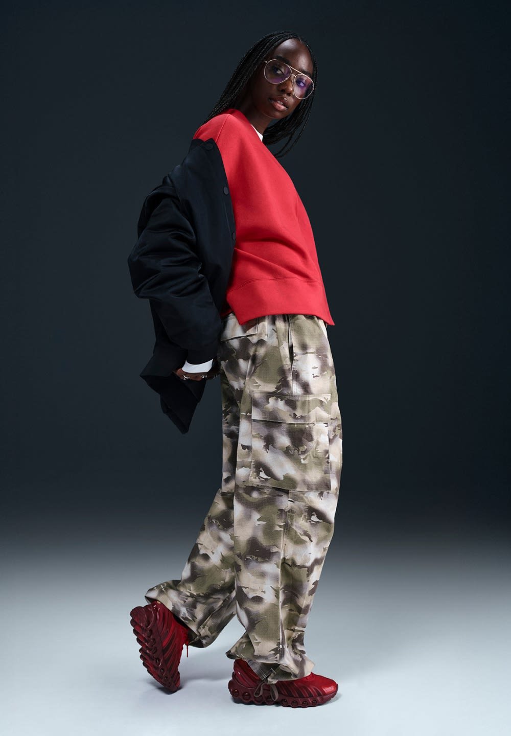 Rode cropped sweatshirt, zwart oversized jack, camouflage cargo broeken en rode sportieve schoenen met textuuroverlagen, die een modern ontwerp aanvullen.