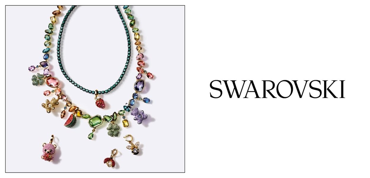 Dwa kolorowe naszyjniki z koralików z zawieszkami w kształcie owoców i zwierząt na białym tle obok logo Swarovski.