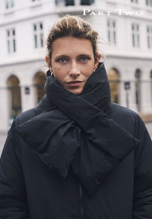 Veste matelassée noire avec un grand col en forme de nœud papillon. Le tissu semble doux, avec une finition mate. Le mannequin porte un maquillage naturel et une coiffure soignée.