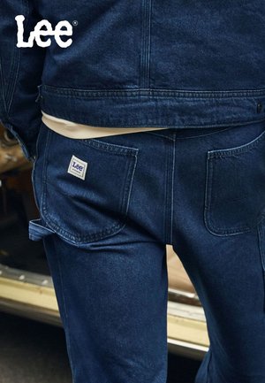 Mørkeblå denimjeans med smal passform, med et logo-patch på baklommen og flate lommer. Glatt tekstur med subtile sømdetaljer.