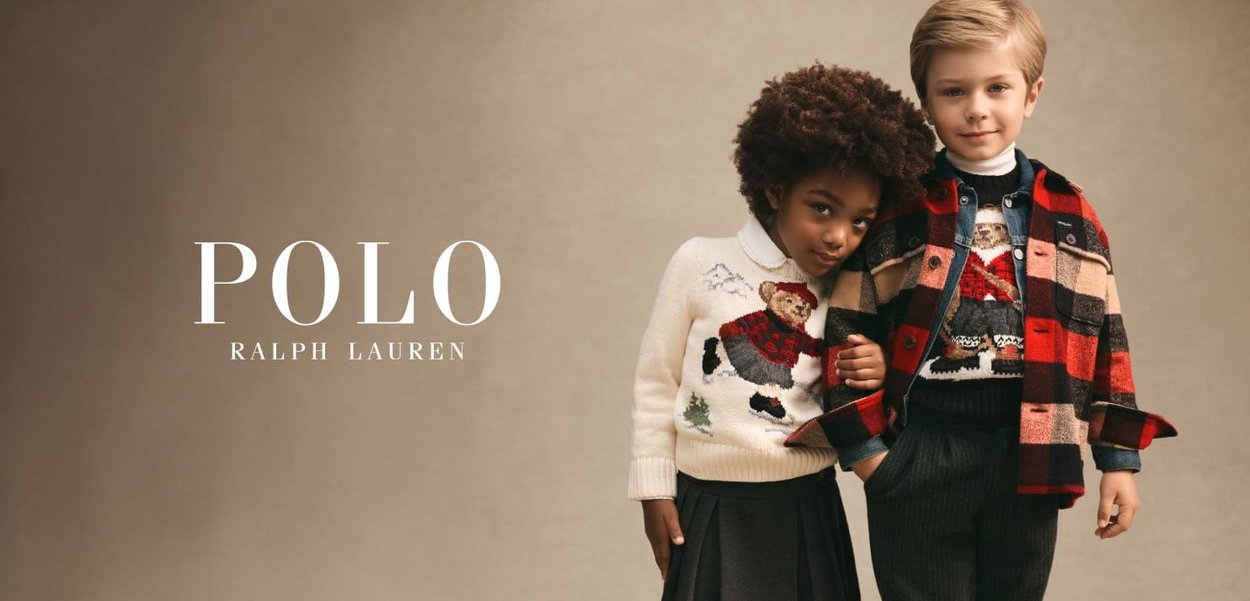 Twee kinderen die feestelijke truien en laagjes kleding dragen, staan zij aan zij tegen een neutrale achtergrond en omhelzen elkaar zachtjes.