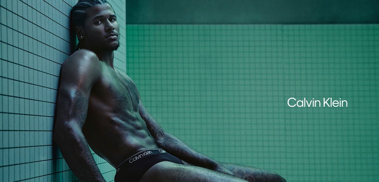Schwarze Calvin Klein Unterwäsche, die auf einem Modell zu sehen ist, das gegen eine grün geflieste Wand lehnt. Der Stoff ist glatt und kontrastiert mit den strukturierten Fliesen.