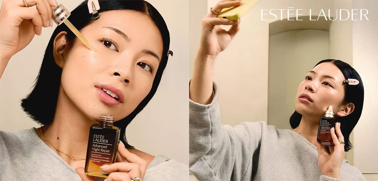 Kvinde påfører Estée Lauder Advanced Night Repair-serum med pipette på sit ansigt og holder produktflasken tæt ved et spejl.