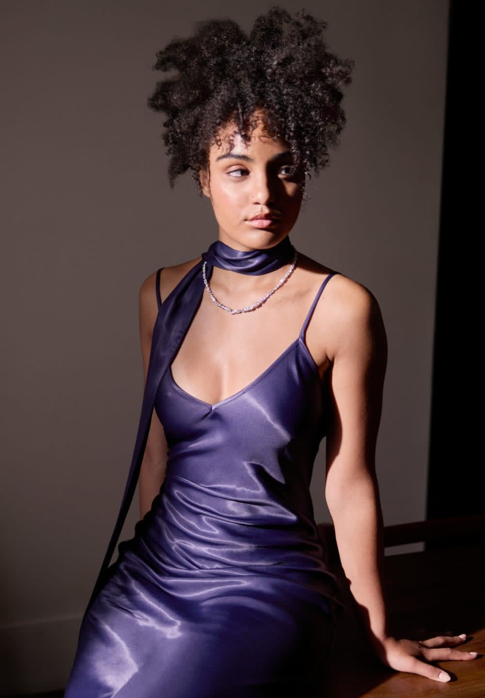 Satin paarse jurk met een diepe V-hals, dunne bandjes en een lange sjaaldetail rond de hals. Subtiele glans en een aansluitende silhouet.