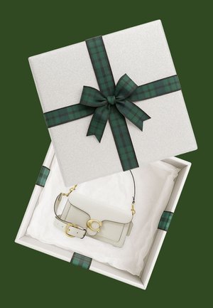 Weiße Lederhandtasche mit goldener Schnalle in einer weißen Geschenkschachtel, umwickelt mit einem dunkelgrünen karierten Band und einer Schleife auf grünem Hintergrund.