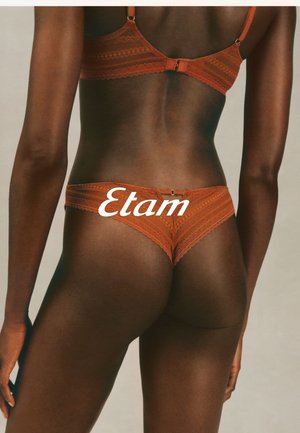 Rust-colored lingerie set made of lace, featuring intricate patterns and adjustable straps on the bra, paired with matching lace panties.