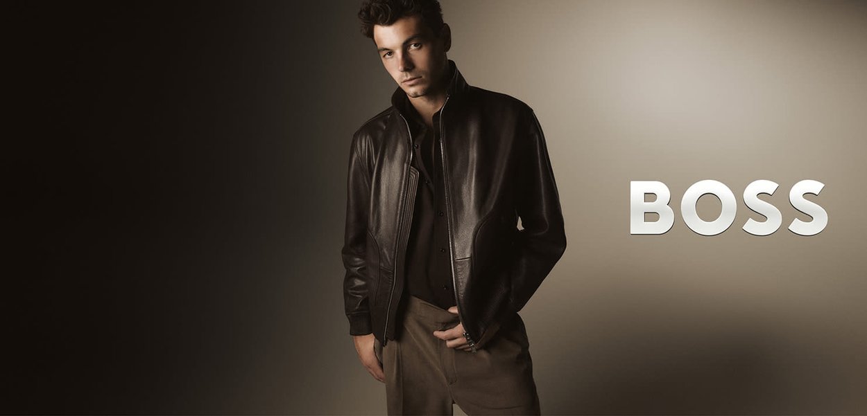 Schwarze Lederjacke mit tailliertem Schnitt, ausgestattet mit einem hohen Kragen und strukturierten Schultern, kombiniert mit einem dunkelknöpfbaren Hemd und beigen Hosen.